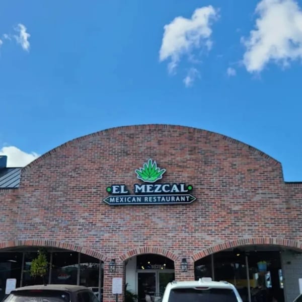 The brick exterior of El Mezcal Mexican Restaurant with its sign and arched windows under a blue sky.