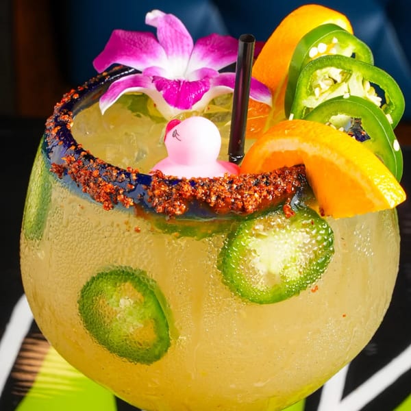 A vibrant El Mezcal Mexican Restaurant margarita with chili-lime rim, orange slices, jalapeños, and a pink rubber duck.