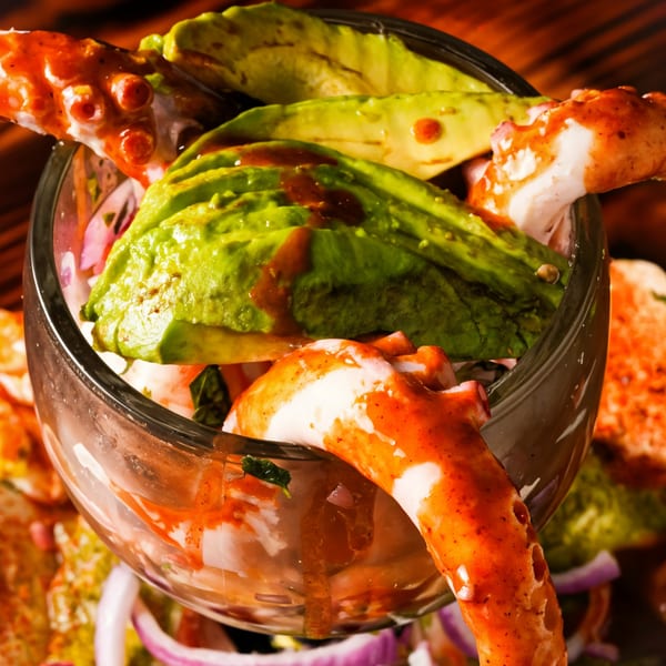 Mexican seafood cocktail with octopus, avocado, and red sauce in a glass.