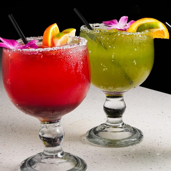Two El Mezcal margaritas, one red and one green, garnished with fruit and flowers.