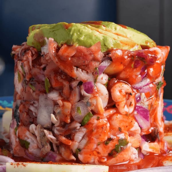 A vibrant Mexican seafood tower with shrimp, octopus, red onions, and avocado, drizzled with red sauce.