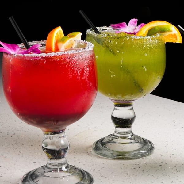 Two vibrant El Mezcal margaritas, one red and one green, garnished with fruit and flowers.